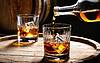 Gießt Whisky aus einer Flasche in ein Glas mit Eiswürfeln | Stock Foto